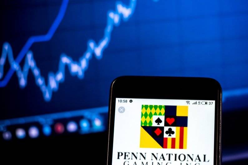 Penn National gaming logo on a smartphone with a stock chart in the background