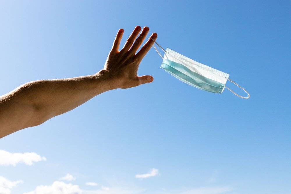 hand holds surgical mask against a blue sky